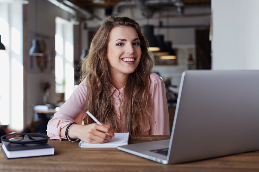 Happy young woman sitting at cafe working remotely